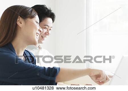 Stock Photo - Young couple sitting on sofa using laptop. Fotosearch