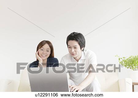 Stock Photograph - Young couple sitting on sofa using laptop. Fotosearch