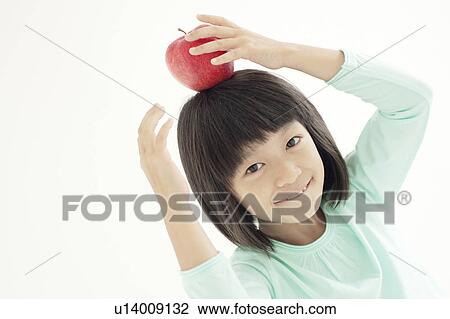 Stock Image - Young Girl Holding Apple on Her Head. Fotosearch