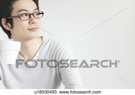 Young man looking away holding a cup View Large Photo Image Stock Image - Young man looking away holding a cup. Fotosearch