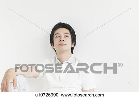 Stock Image - Young man sitting and looking away. Fotosearch