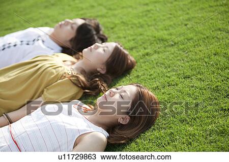 Young people lying down on grass View Large Photo Image Stock Image - Young people lying down on grass. Fotosearch
