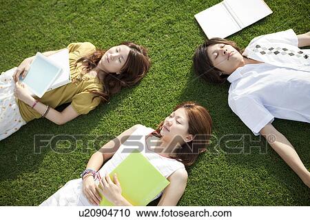 Stock Image - Young people lying down on grass. Fotosearch