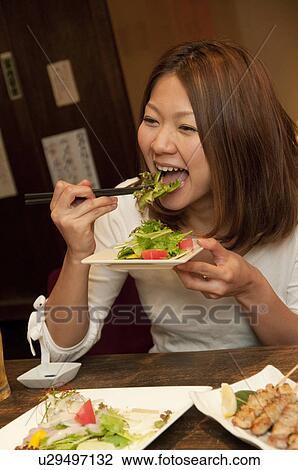 Stock Image - Young woman eating salad at a bar. Fotosearch