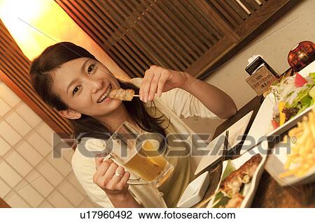 Stock Image - Young woman eating Yakitori (Chicken Kebabs ). Fotosearch