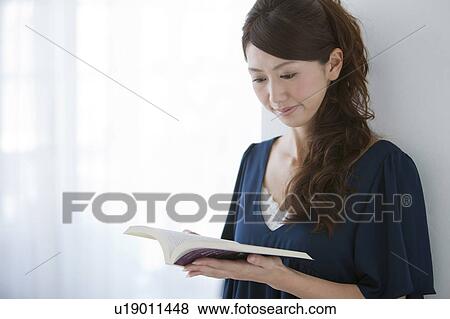 Stock Photo - Young woman leaning on wall and reading book. Fotosearch