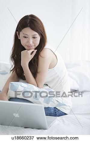 Stock Photo - Young woman sitting on bed using laptop. Fotosearch