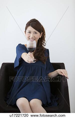 Stock Image - Young woman sitting on chair holding glass of wine. Fotosearch