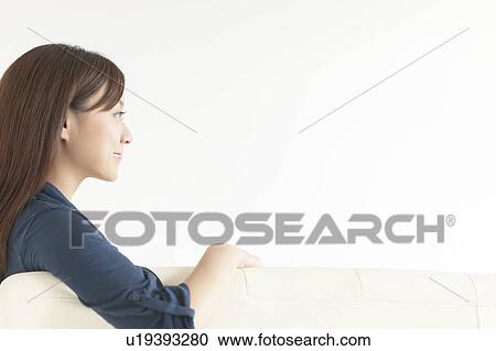 Stock Image - Young woman sitting on sofa. Fotosearch