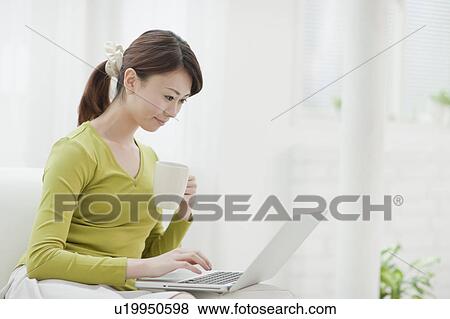 Stock Photo - Young Woman Using Laptop and Having Drink. Fotosearch