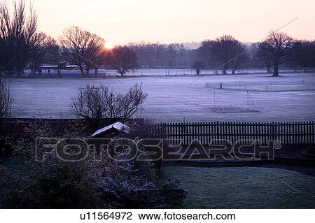 Aerial view of snowy fields at sunrise, England, with wooden fenced garden in foreground, and sun rising behind trees along edge of school football field. View Large Photo Image Stock Image - Aerial view of snowy fields at sunrise, England, with wooden fenced garden in foreground, and sun rising behind trees along edge of school football field.. Fotosearch