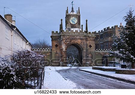 Stock Image - Bishop's Palace: view of clock tower, arched entranceway to Bishop's Park in late afternoon sunlight, winter with snow and blue sky, Bishop Auckland, Northern England. Fotosearch
