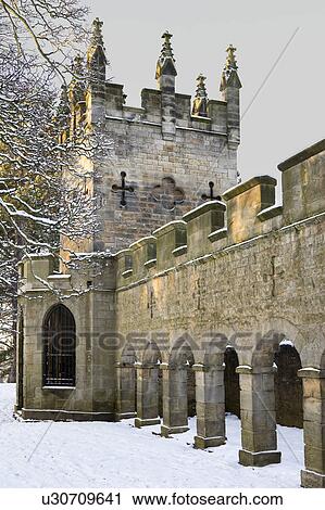 Stock Image - Deer Shelter, built 1780 in medieval style, stone wall with crenellations, arched columns, tower with spires, snowy winter in late afternoon sunshine, Bishop Auckland, Northern England. Fotosearch