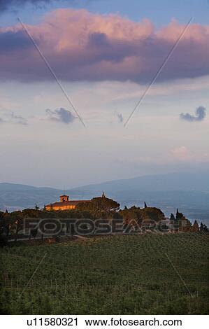 Stock Image - Italian rural abbey at sunset, with spectacular cloud formation, vineyards on sloping hills of foreground. Fotosearch