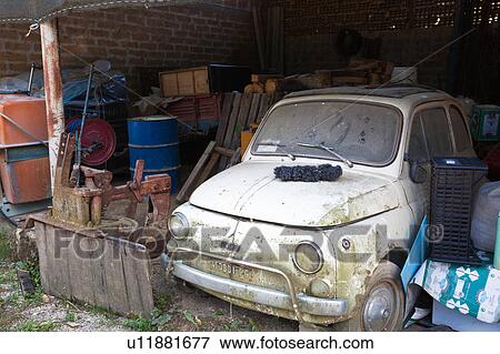 Stock Photo - Old, white, dusty Fiat 500 parked in old barn, surrounded by farming equipment, Umbria, Italy. Fotosearch