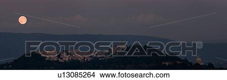 Picture - Panorama view of full moon rising over medieval hilltop town of Todi, with spire of San Fortunato, and Tempio of Bramante, town lights illuminated at dusk, Umbria, Italy. Fotosearch