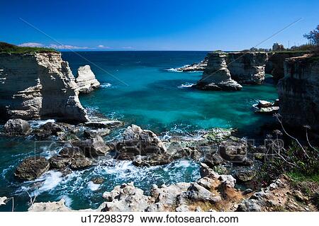 Stock Photo - Rocky coastline and natural arch formation of sea stacks, clear blue sea on sunny spring morning, Salento, Puglia, Southern Italy. Fotosearch