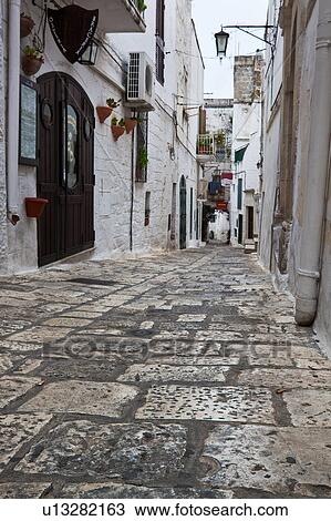 Street in Ostuni, with typical white stucco walls, stone paving, wrought iron lamp, and archway, with flowers decorating, spring afternoon, Salento, Puglia, Southern Italy View Large Photo Image Stock Image - Street in Ostuni, with typical white stucco walls, stone paving, wrought iron lamp, and archway, with flowers decorating, spring afternoon, Salento, Puglia, Southern Italy. Fotosearch