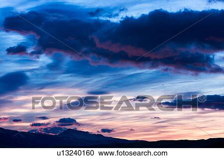 Stock Image - Sunrise with dramatic blue grey clouds, pink tinged edges, hills silhouetted, Torres del Paine, Southern Chile, Patagonia. Fotosearch