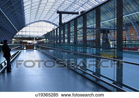 Stock Photography - Upper concourse of St. Pancras International railway station, London, England, showing glass and metal domed ceiling, platforms, with stationary train, and solitary waiting passenger. Fotosearch