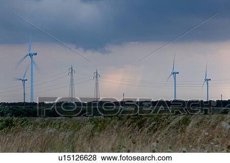 Stock Photo - Wind turbines and electricity pylons against stormy grey sky at sunset, Salento, Puglia, Southern Italy. Fotosearch