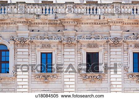 Stock Photography - Window detail: ornate Baroque facade of Palazzo del Seminario, with balustrade above, ornately carved in Leccese style, reflection of blue sky in glass, Lecce, Salento, Puglia, Southern Italy. Fotosearch