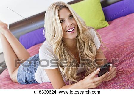Beautiful woman lying on bed with mobile phone View Large Photo Image Picture - Beautiful woman lying on bed with mobile phone. Fotosearch