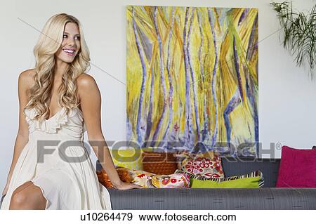 Stock Photo - Beautiful young woman looking away with painting in background. Fotosearch