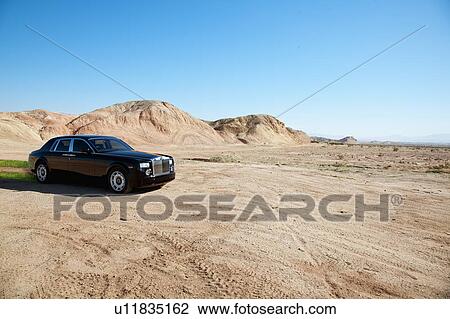 Stock Image - Black eco-friendly Rolls Royce car running off-road on unpaved road. Fotosearch