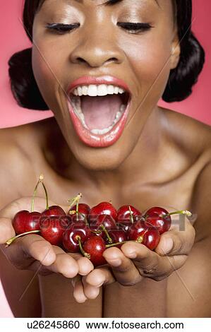 Stock Image - Cheerful young woman looking at cherry in her hands. Fotosearch
