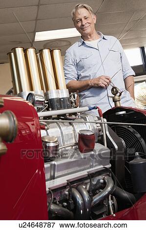 Stock Photo - Close up of car engine with happy senior man standing behind. Fotosearch