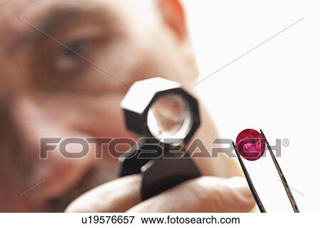 Stock Photo - Close up of gemstone with jeweler looking through magnifying glass. Fotosearch
