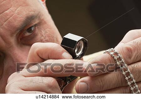 Picture - Close up of man looking at jewelry through magnifying glass. Fotosearch