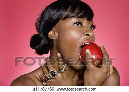 Stock Image - Close up of woman biting an apple over colored background. Fotosearch