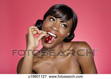 Stock Photo - Close up of woman eating cherry over colored background. Fotosearch