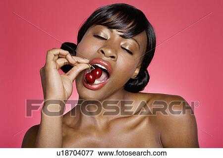 Stock Photo - Close up of woman eating cherry with eyes closed. Fotosearch