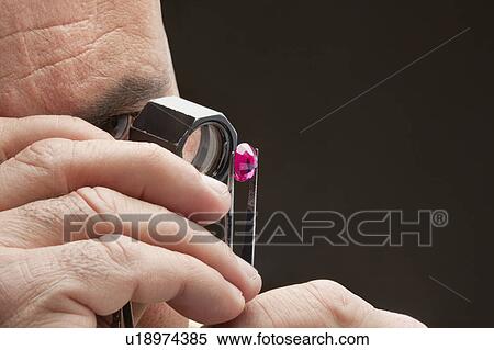 Stock Photography - Cropped image of jeweler examining jewel over black background. Fotosearch