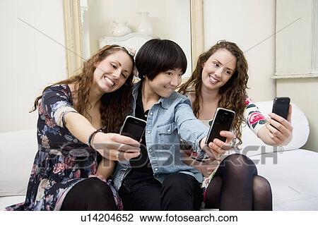 Stock Image - Female friends taking self photograph. Fotosearch