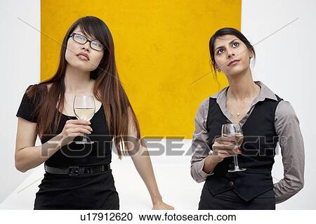 Stock Image - Front view of young females with wine glass looking up in art gallery. Fotosearch