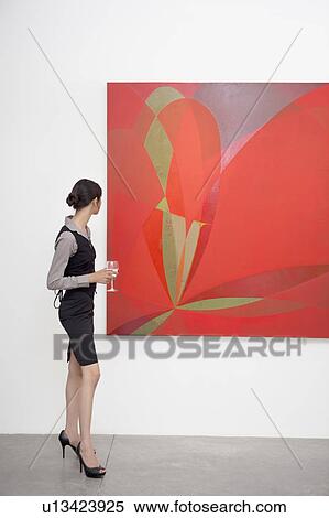 Stock Photography - Full length of a woman looking at painting in art gallery. Fotosearch