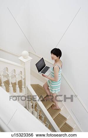Full length of young woman with laptop walking up stairway View Large Photo Image Stock Photograph - Full length of young woman with laptop walking up stairway. Fotosearch