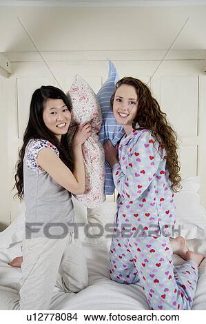 Happy female friends having pillow fight View Large Photo Image Picture - Happy female friends having pillow fight. Fotosearch