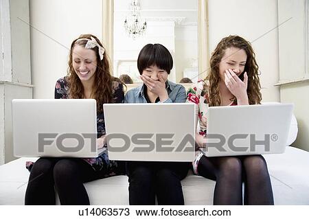 Laughing young female friends sitting on sofa View Large Photo Image Stock Image - Laughing young female friends sitting on sofa. Fotosearch