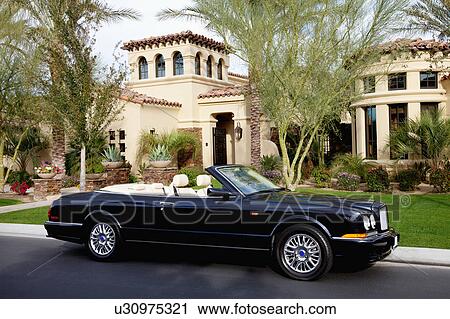 Stock Image - Luxurious convertible car parked in front of a mansion house. Fotosearch