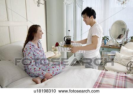 Stock Image - Man bringing wife breakfast in bed. Fotosearch