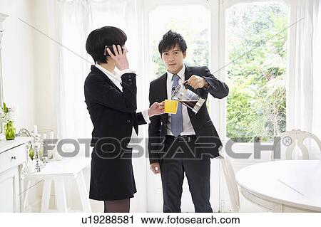 Stock Image - Man pouring tea while woman on call. Fotosearch