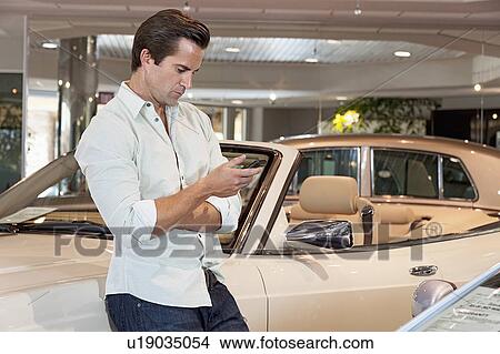 Picture - Man standing besides car with his mobile phone. Fotosearch