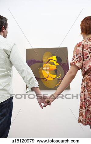 Married couple holding hands in front of painting in art gallery View Large Photo Image Stock Photo - Married couple holding hands in front of painting in art gallery. Fotosearch
