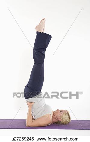 Stock Photography - Mature woman doing a yoga pose with feet in the air. Fotosearch