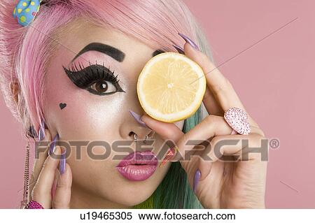 Stock Photography - Portrait of a woman holding slice of lime in front of her eyes. Fotosearch